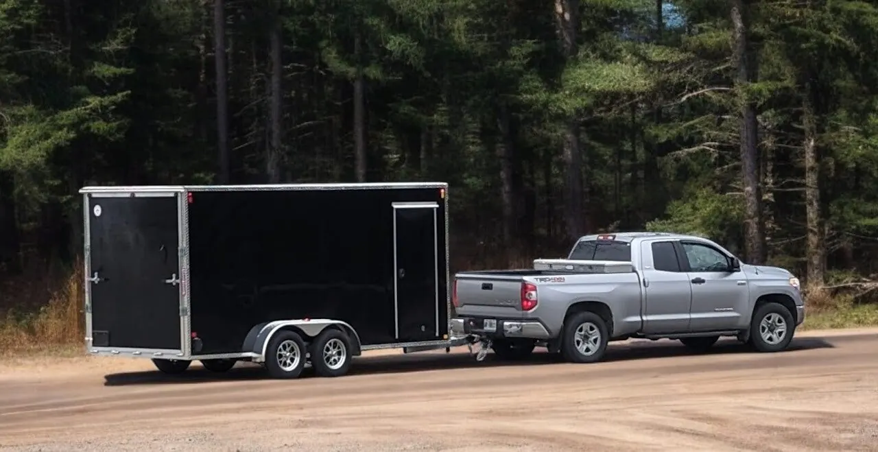 Black Allen & Alloy enclosed tandem trailer hitched to a pickup on a gravel road