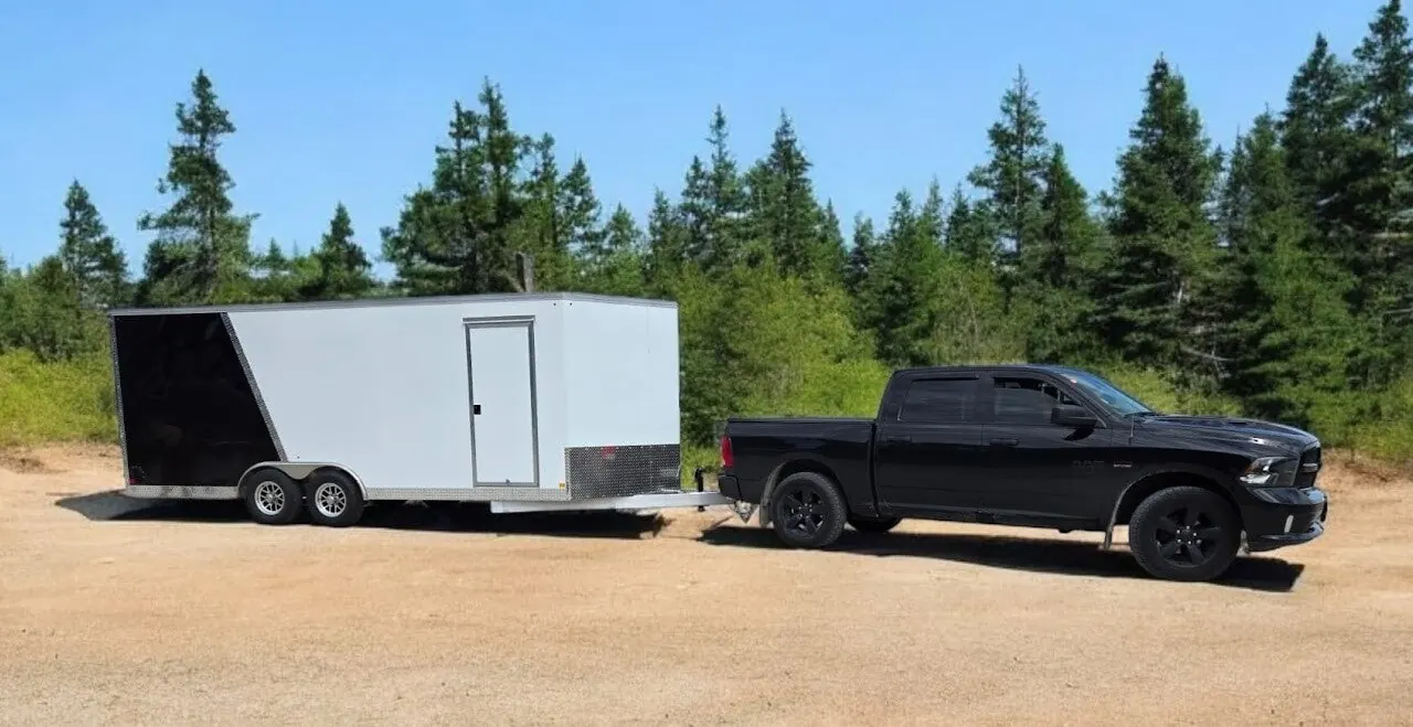 White enclosed trailer towed by a pickup on a forest road